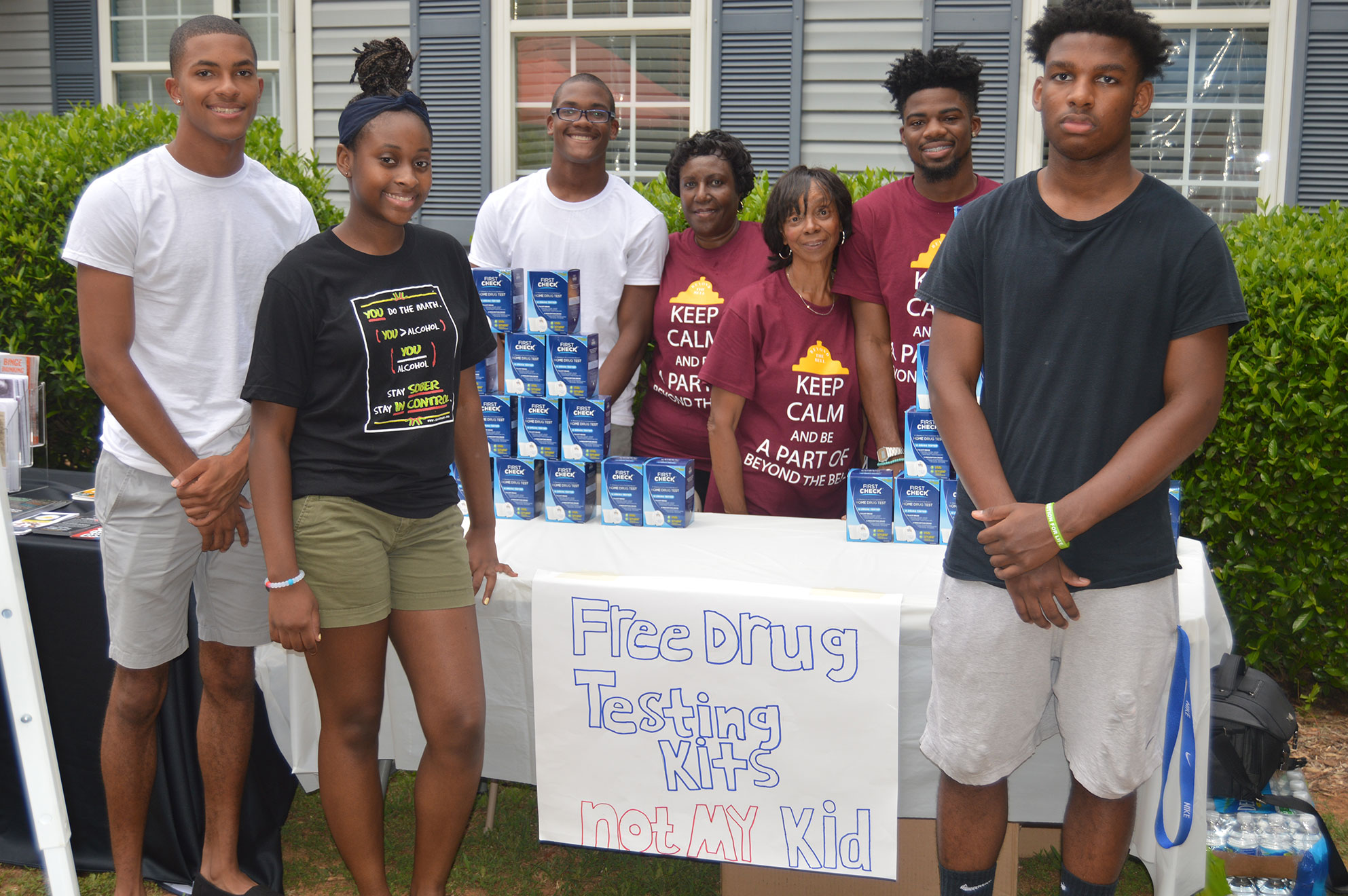 Seven people stand around a table with drug tests and a sign saying "Free Drug Testing Kits Not My Kid"