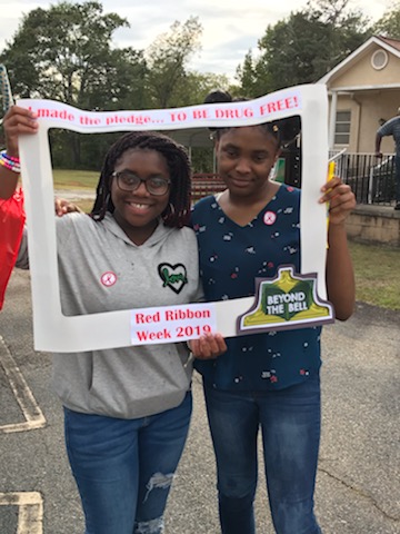 Two teenage girls pose with a sign saying "I made the pledge to be drug free! Red Ribbon Week 2019."
