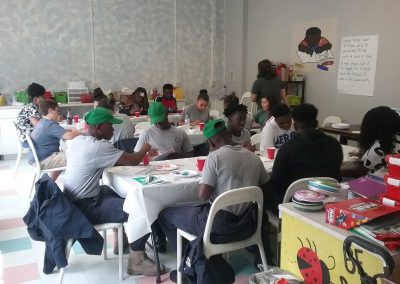 Children and teenagers sit at tables painting.