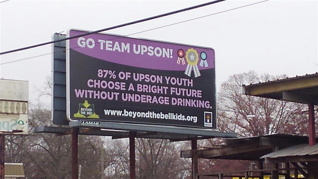 A black and purple billboard that says "Go Team Upson! 87% of Upson youth choose a bright future without underage drinking."