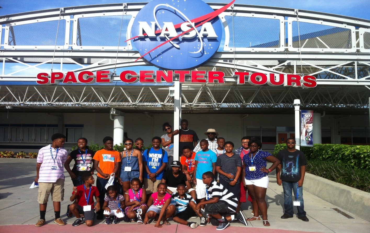 A group of African American children and adults stand under a "NASA Space Center Tours"  sign.