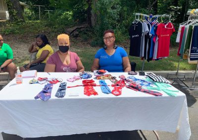 Two woman sit at a table selling ties and t-shirts.