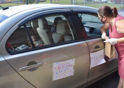 A woman looking in a car window. The car is decorated with hand-drawn signs that say "Be happy" and "Be brave."