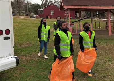 Four teenagers wearing yellow vests. Two of them are carrying empty orange garbage bags.